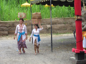 Women carry nearly everything on their heads.  In this case, they are carrying offerings to the temple on their heads, because the head is the most sacred part of the body.  So, not only is the head a good place to carry stuff, it's respectful to their worship.